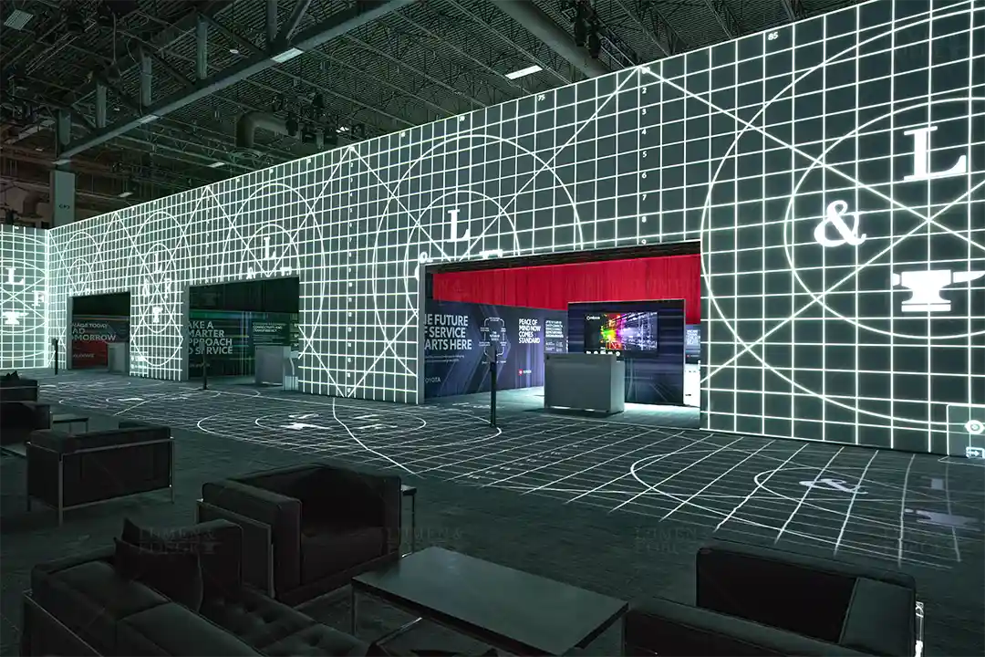 Tradeshow booth with white grid lines and a brand logo projection mapped across the walls and floor, lounge seats in front