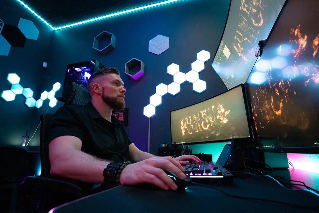 Animator at a neon-lit battlestation with hexagon wall lights and monitors showing a fiery Lumen and Forge logo