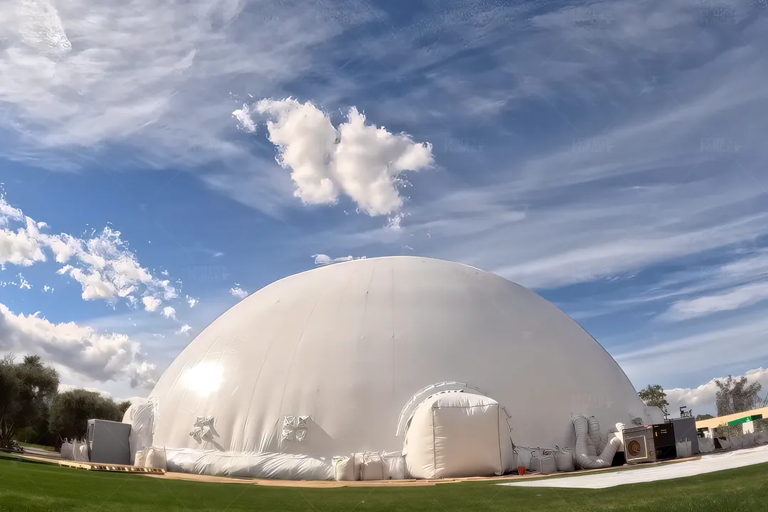 White inflatable pop-up dome with an entry tunnel set up on a lawn under a blue sky for the AUG trade show