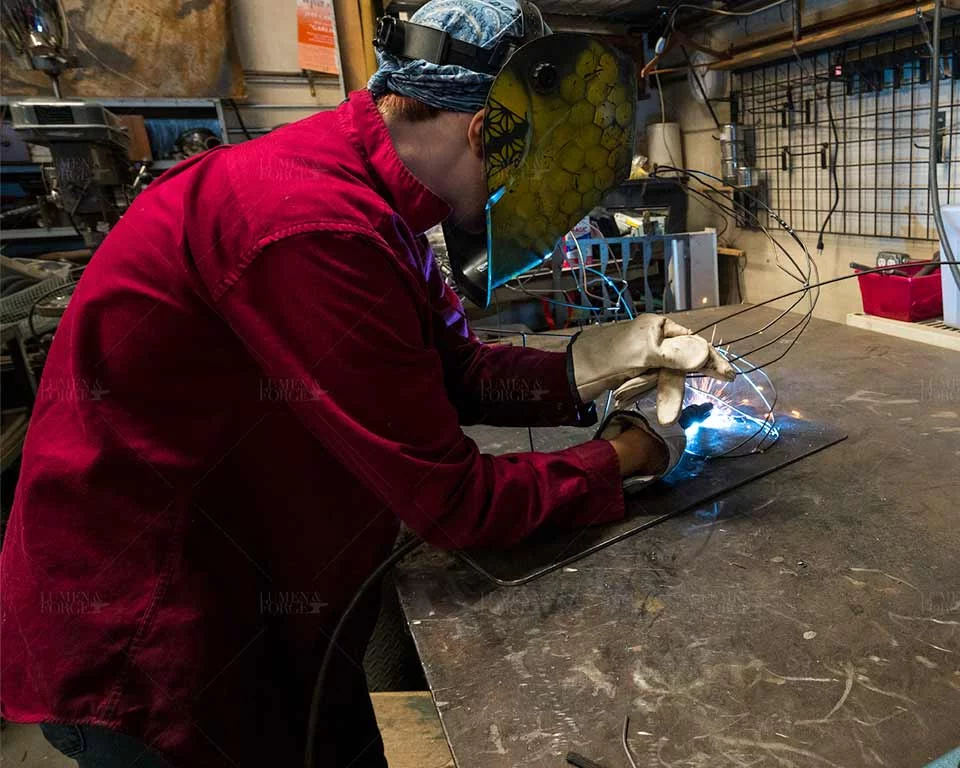 Artist welding a reclaimed-material sculpture for the Beneath the Blue exhibit