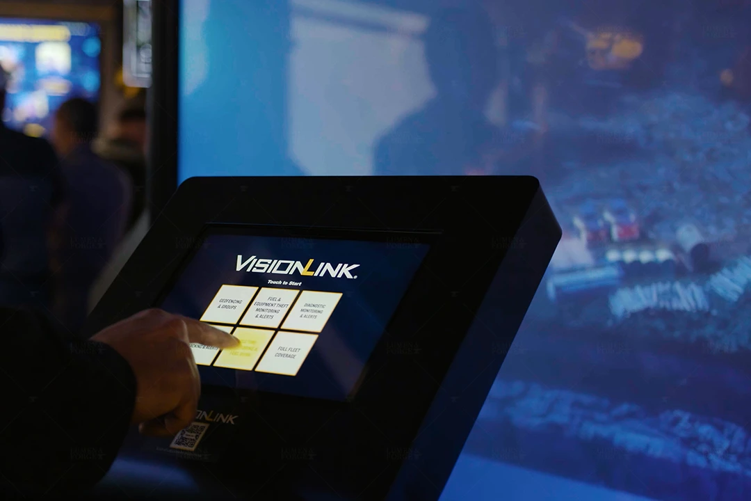 Visitor taps a VisionLink touchscreen menu in front of a projected construction scene at the Caterpillar Con Expo booth