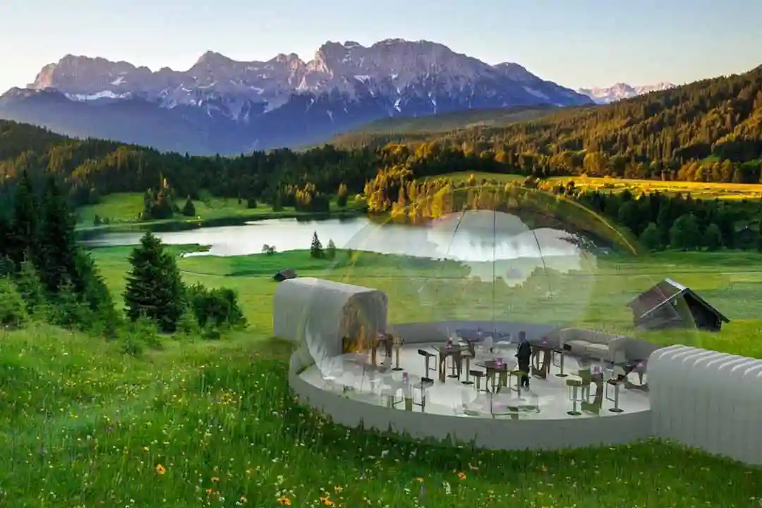 3D visualization of a clear outdoor dining dome in an alpine meadow with a lake and snowy mountains behind