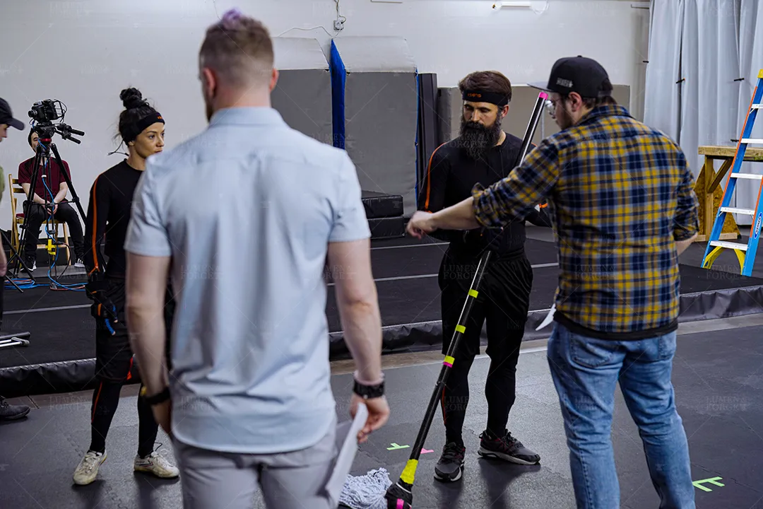 Motion capture session with performers in mocap suits and crew preparing a marker-tracked prop pole