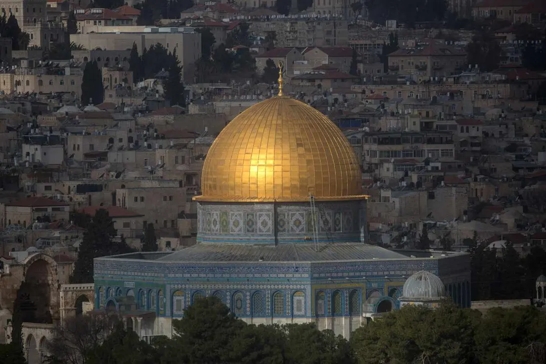 Golden dome atop an octagonal shrine with blue tilework, surrounded by the stone buildings of an old city