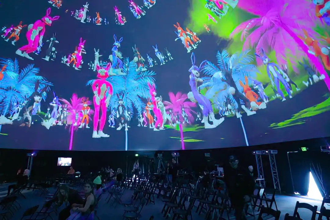 Projection dome at SXSW filled with neon rabbits and palm trees above rows of chairs and a few guests