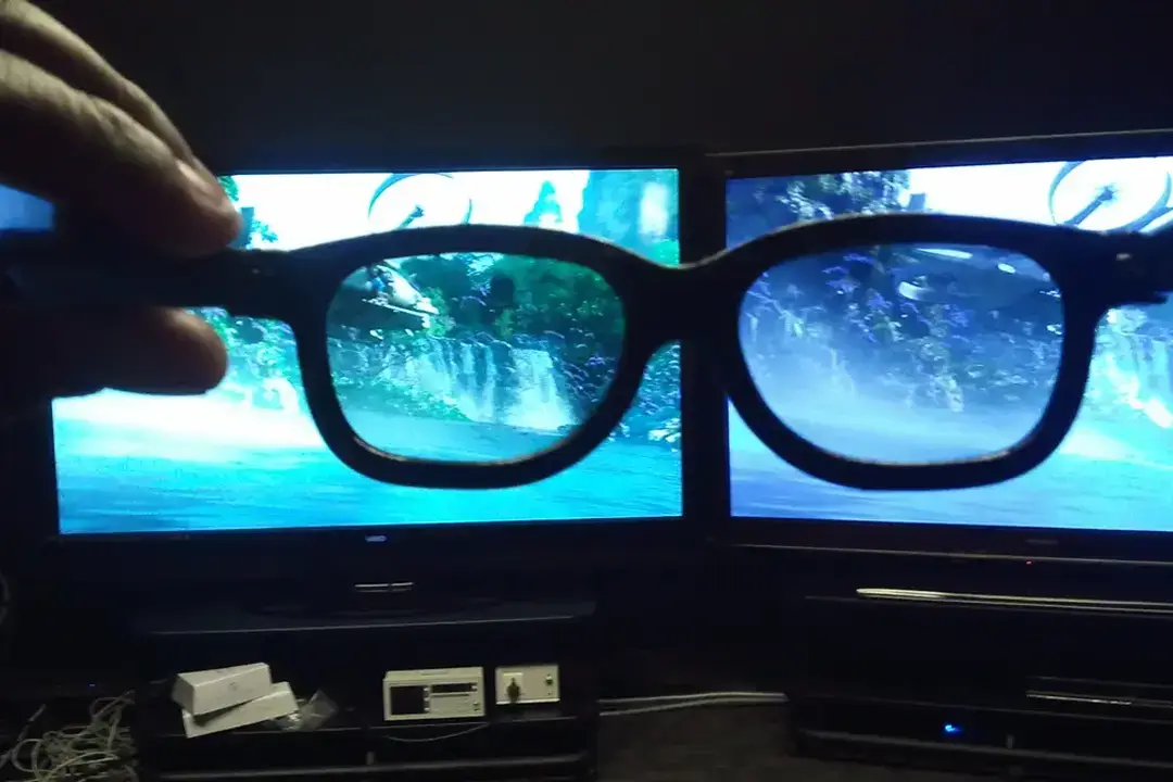 Hand holding 3D glasses in front of two TV screens showing a jungle waterfall scene