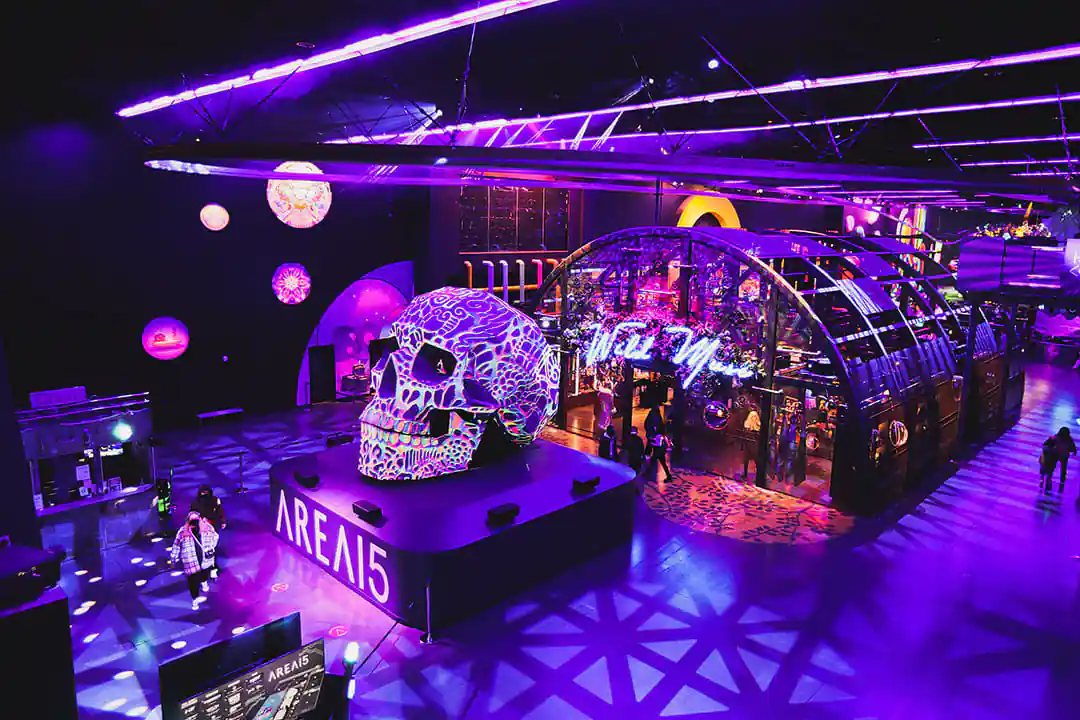 AREA15 main floor bathed in purple light, with a neon patterned skull sculpture on a stage marked AREA15