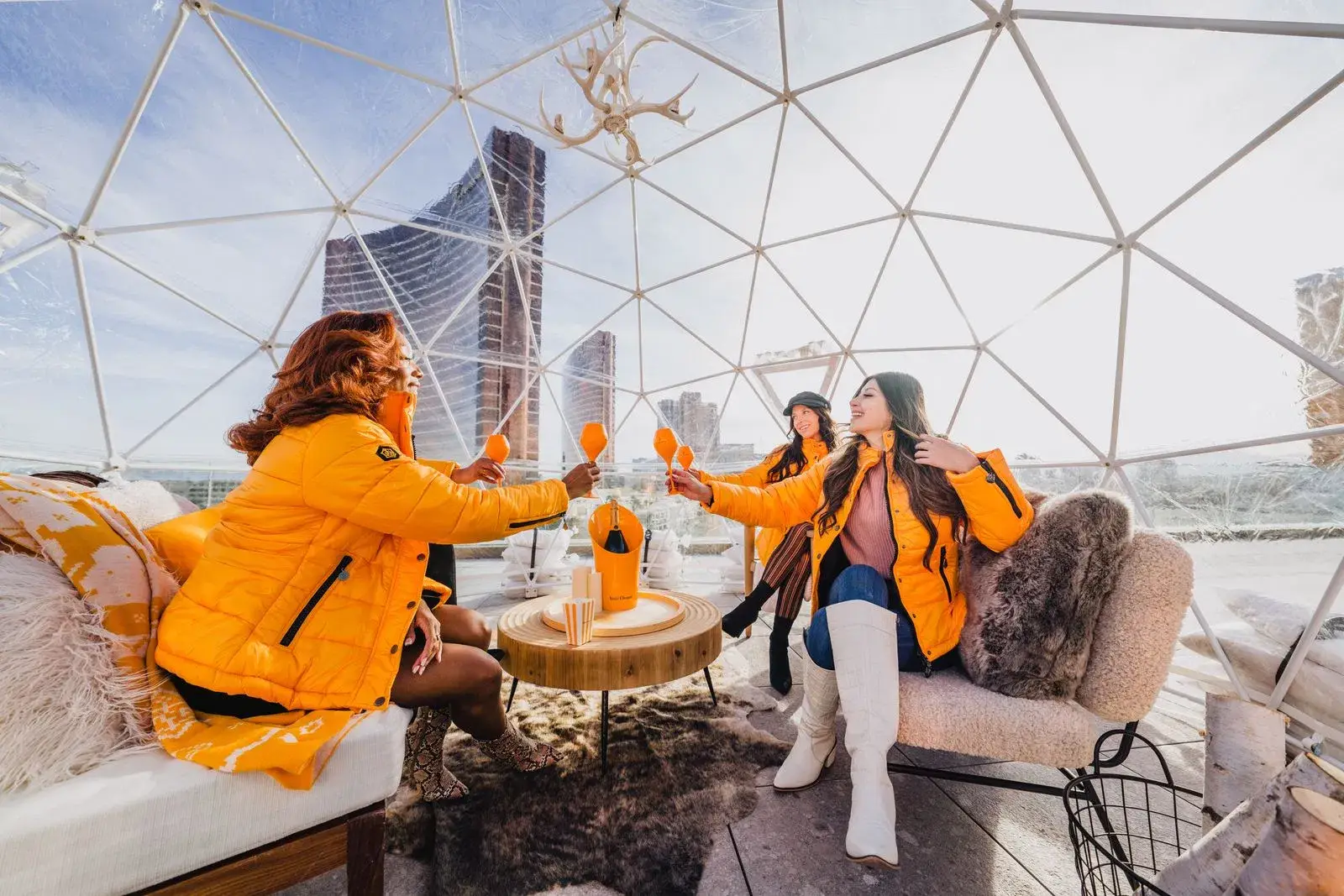 Women in yellow puffer jackets toasting inside a clear geodesic dome at the Rose Rooftop, Resorts World