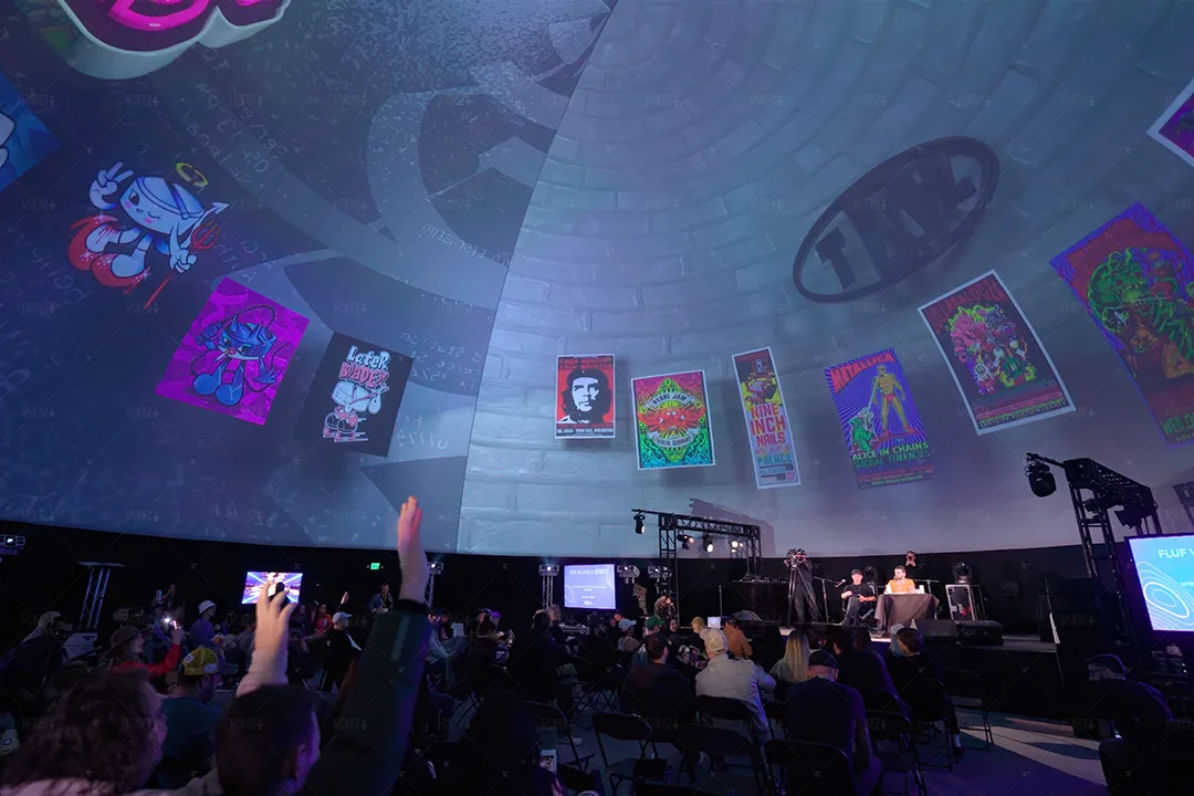 Audience with raised hands inside a convention dome projected with colorful poster art above a panel stage at SXSW