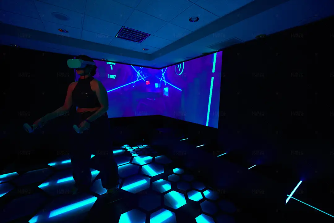 Woman in a VR headset playing a rhythm game on projected walls in a dark room with a glowing blue hexagon floor