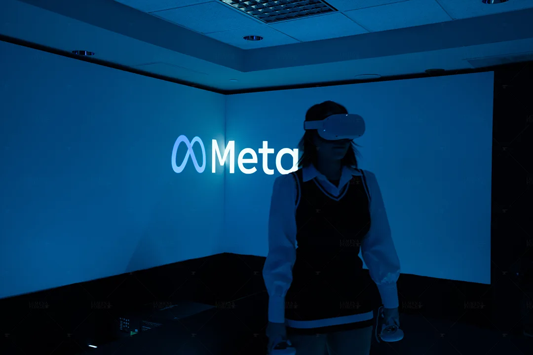 Woman in a VR headset in a blue-lit room with the Meta logo projected on the wall, at the Latin Grammys VR experience