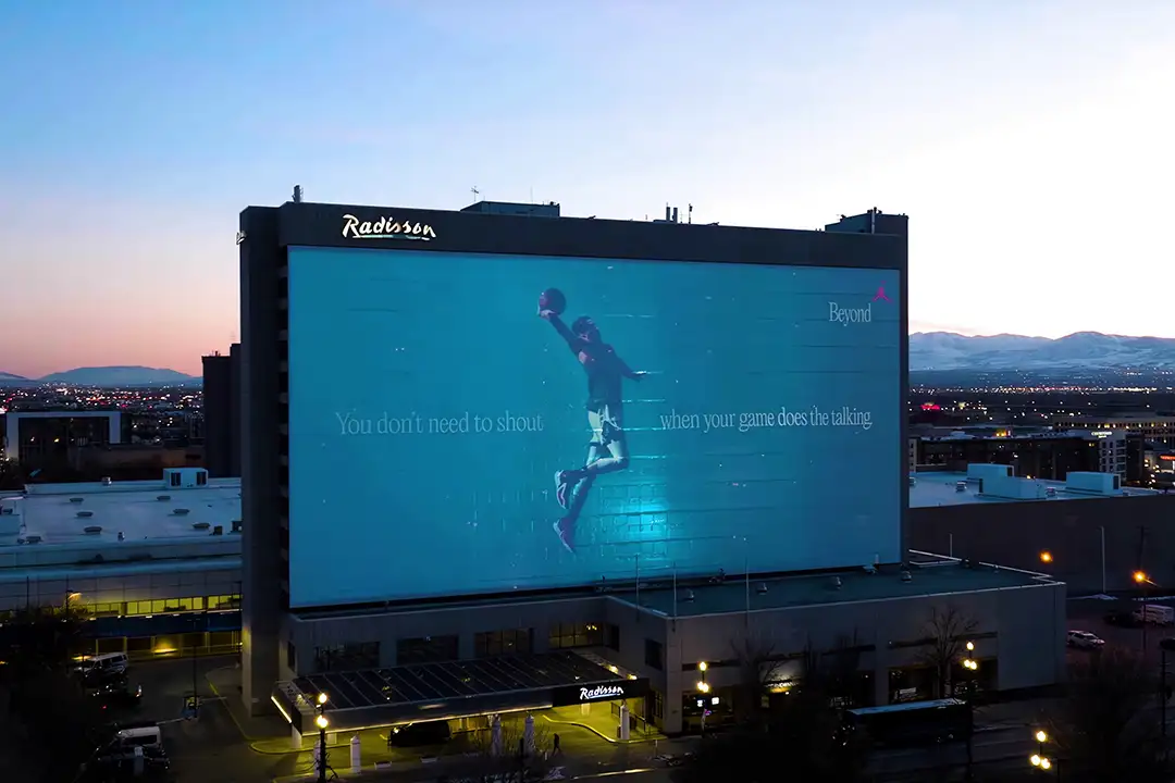 Nike Beyond ad projected on a Radisson hotel facade at dusk, reading 'You don't need to shout when your game does the talking'