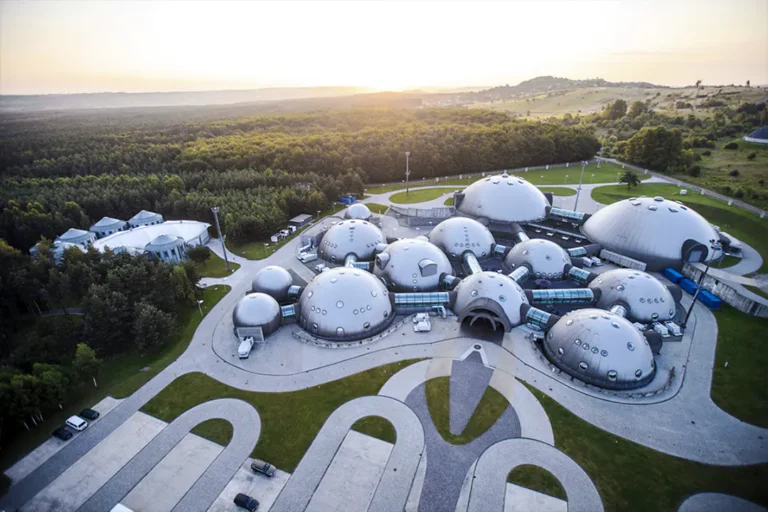 Aerial rendering of a futuristic facility of connected silver domes surrounded by forest at sunset
