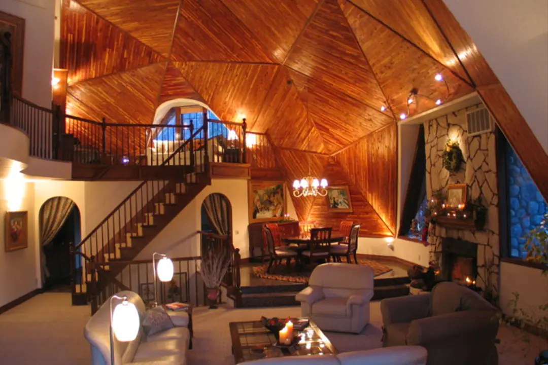 Geodesic dome home interior with a wood-paneled ceiling, loft staircase, stone fireplace and living room seating