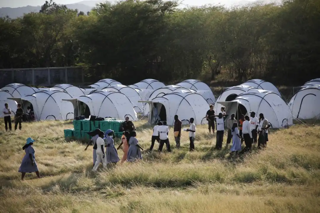 Rows of white emergency shelter domes in a grassy field in Haiti with people walking between them