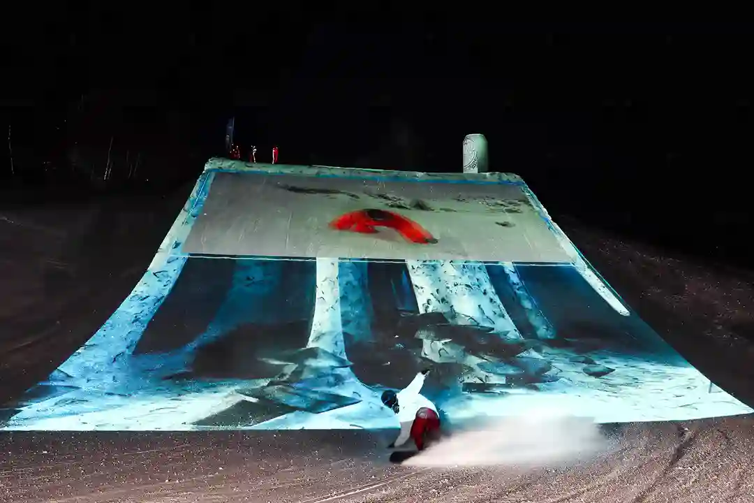 Snowboarder riding past a projection-mapped snow ramp at night during a Samuel Adams experiential event