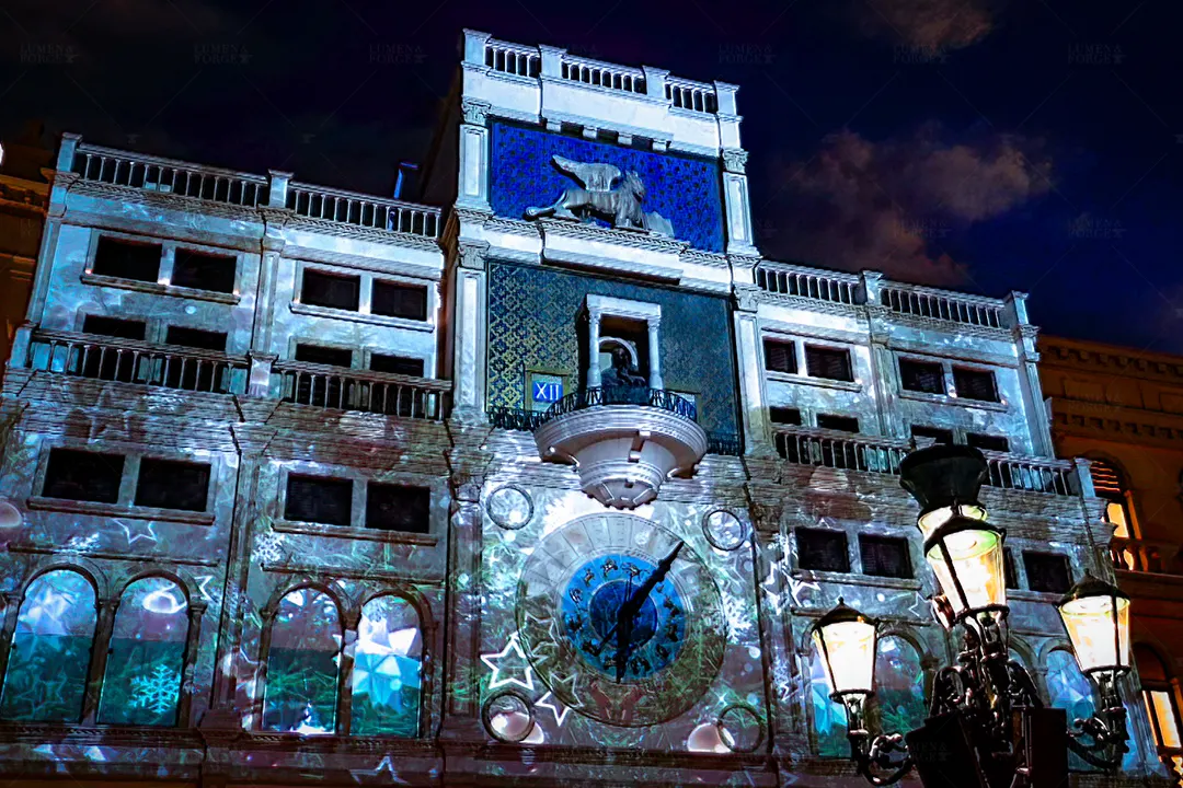 Clock tower facade covered in projected snowflakes and stars, with winged lion and clock face, at St. Mark's Square