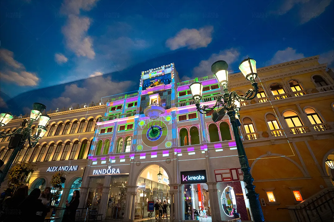 Clock tower at St. Mark's Square projection-mapped in purple, green and blue above Pandora and Alex and Ani storefronts