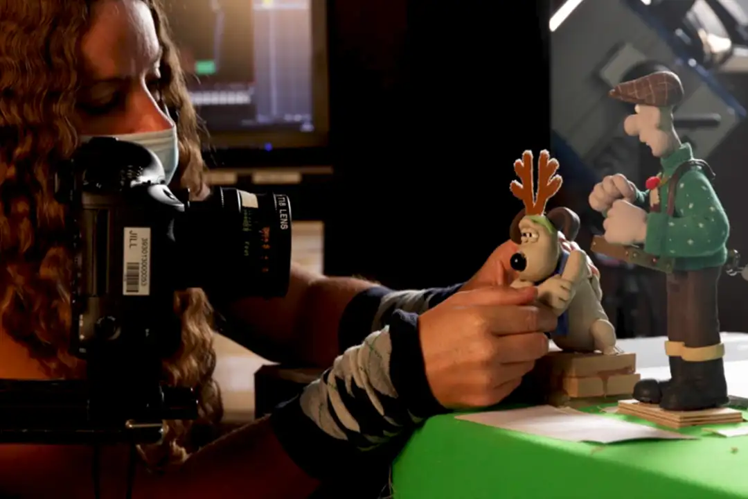 Stop motion animator with a camera posing clay Wallace and Gromit figures, Gromit wearing antlers, on a green table