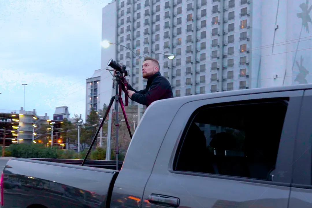 Photographer with a tripod-mounted camera in a pickup truck bed at dusk, capturing the Tropicana hotel tower for photogrammetry
