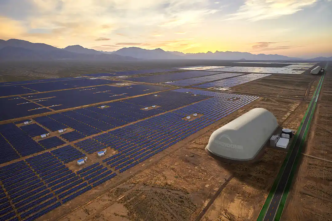 Aerial view of a large white Energy Dome storage building beside vast solar panel fields in the desert at sunset