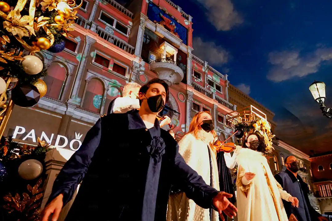 Singers in face masks and a violinist perform the Holiday Spectacular beneath the projection-mapped clock tower at St. Mark's Square