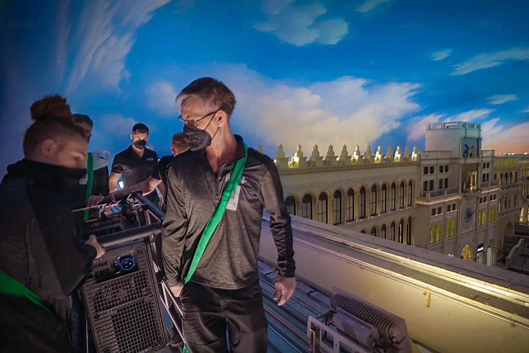 Projection crew in face masks adjusting equipment on a rooftop, with the St. Mark's Square clock tower behind, at The Venetian