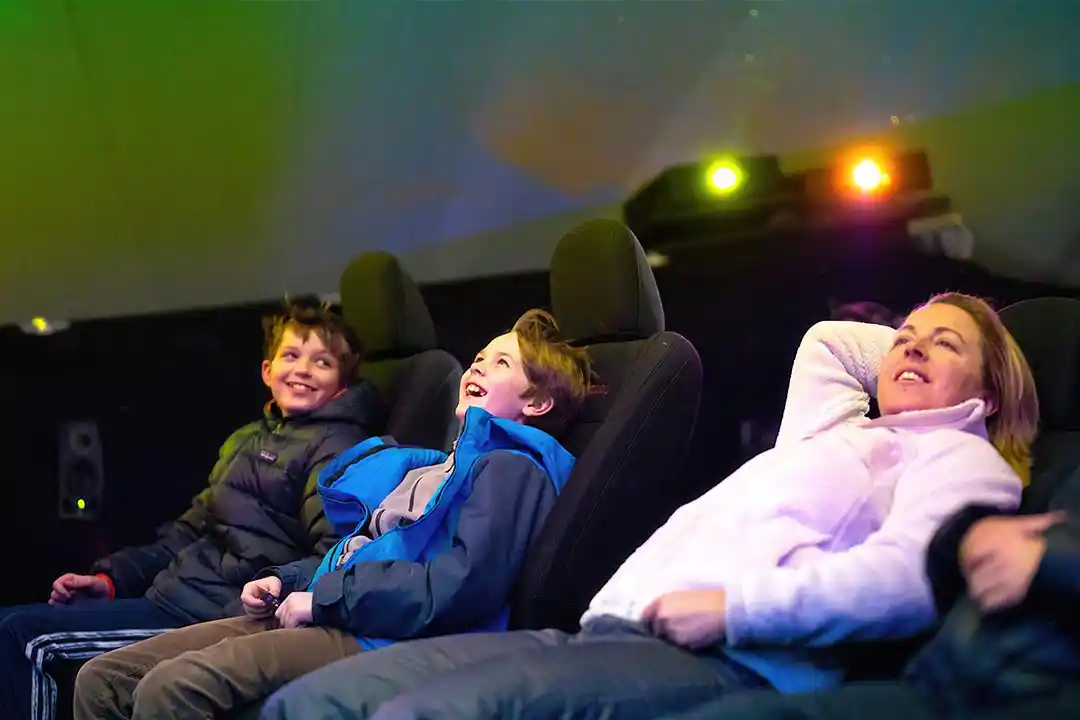 Family laughing in reclined seats inside the Jeep 4D dome theater, looking up at the projected dome screen