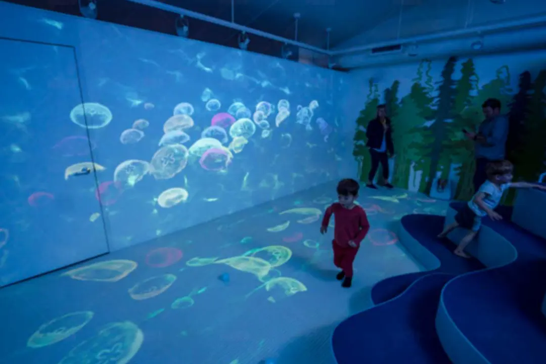 Children playing at the Wild Child Children's Museum, jellyfish projected across the walls and floor