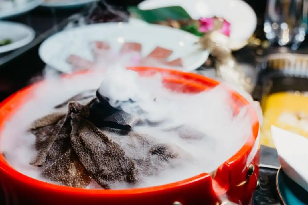 Red pot of dark sliced ingredients shrouded in dry ice fog, a steaming food presentation at The X Pot Chicago