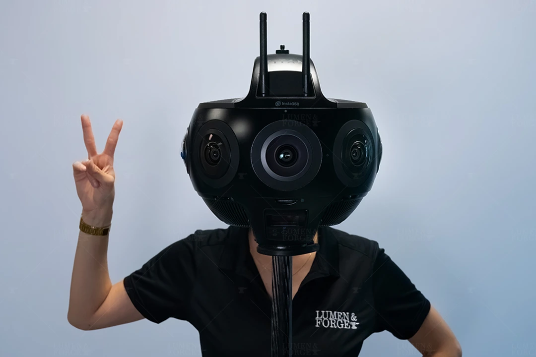 A person hides their head behind a Titan 360 camera to give the illusion the person has a giant camera-head. They are posing with a two-finger peace sign looking like a cyborg-droid.