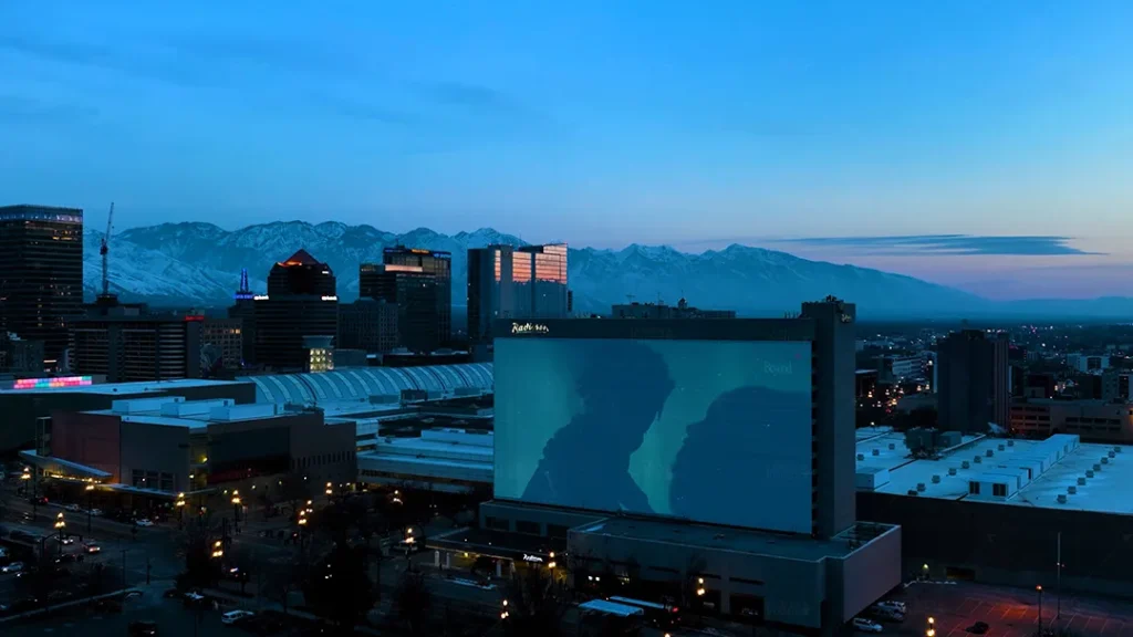 A large-scale projection mapping display on a building in downtown Salt Lake City, Utah, showcasing a Nike advertisement during the NBA All-Star Game. The projection features a dynamic image of two athletes, creating a striking visual against the twilight skyline with the Wasatch mountain range in the background.