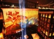 A vibrant projection mapping display illuminates a historic brick building in New York City, featuring dynamic red and blue imagery of a tree and waves. The visual spectacle draws a large crowd of onlookers, showcasing the transformative power of projection mapping in an urban setting.