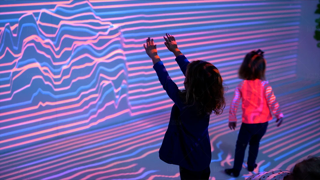 Children interacting with a colorful, immersive projection display at the Wild Child Interactive Museum in the Bay Area, California. The exhibit features dynamic, wavy lines in vibrant colors, engaging the kids in an interactive experience.