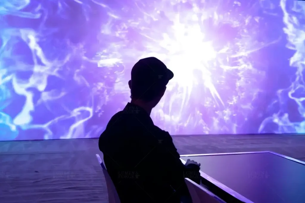 A person sits in front of a large-scale projection mapping display at a Toyota tradeshow event. The screen features an intense burst of purple and white energy-like visuals, creating an immersive, futuristic ambiance. The silhouette of the individual is sharply contrasted against the vibrant background, emphasizing the scale and impact of the digital experience.
